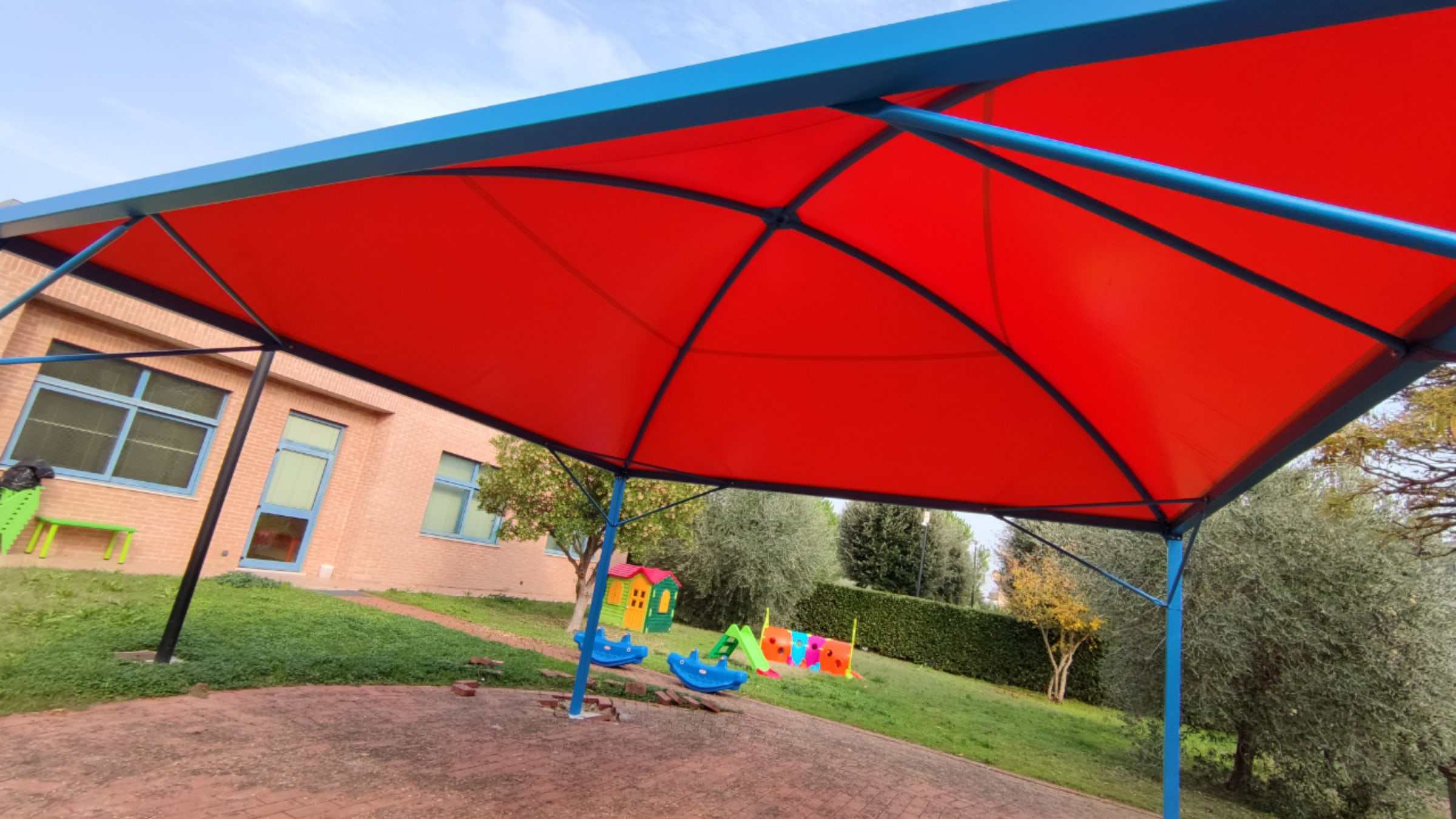 Copertura a telo rosso con struttura blu nel giardino di una scuola