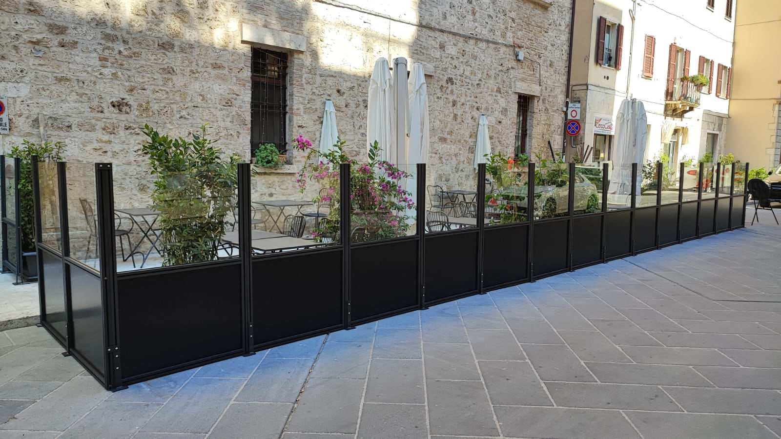 Dehors delimitato da paraventi in vetro su una piazza lastricata