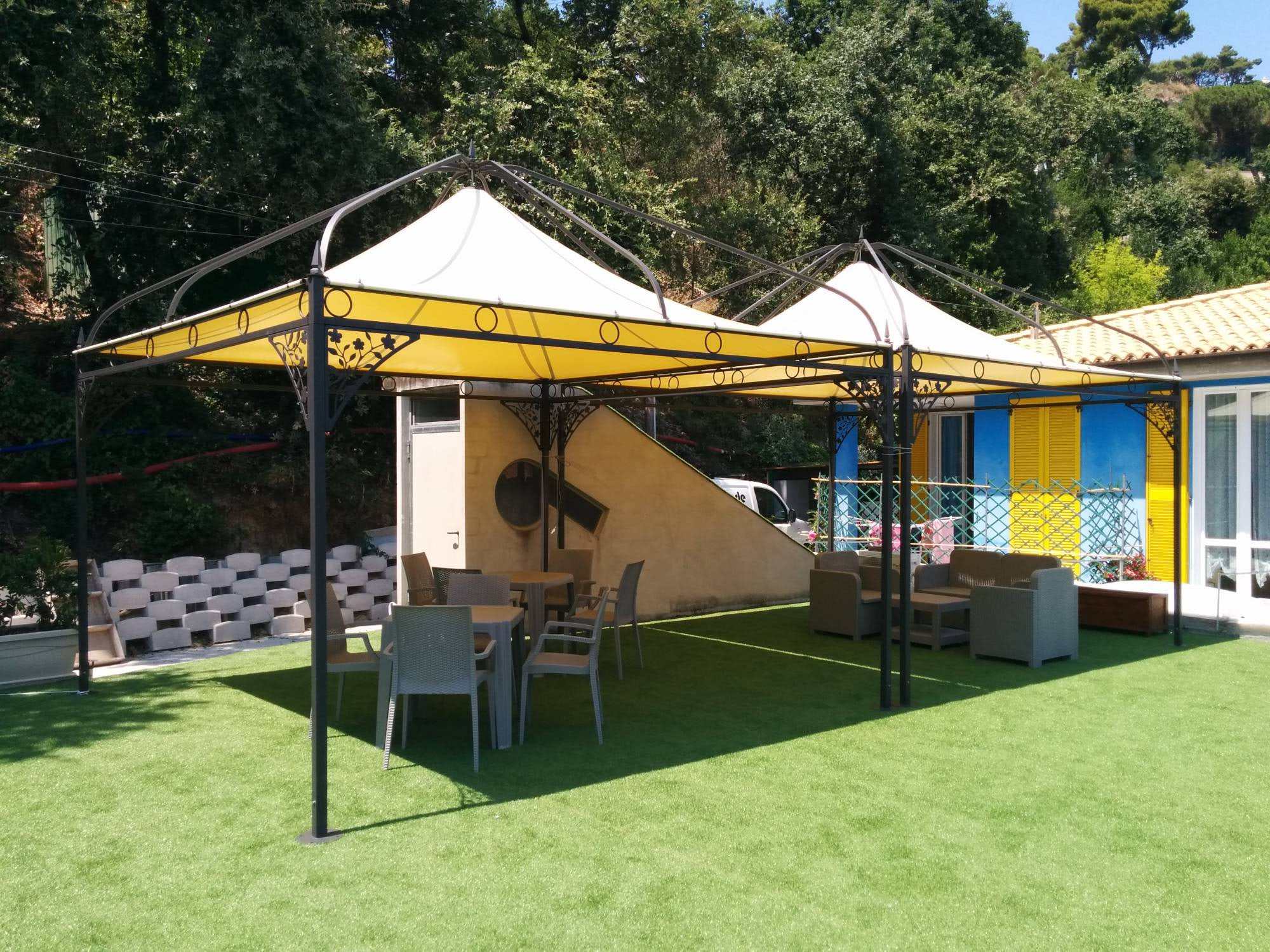 Due gazebo in ferro battuto con telo bianco e giallo su un prato con tavoli e salotto da esterno