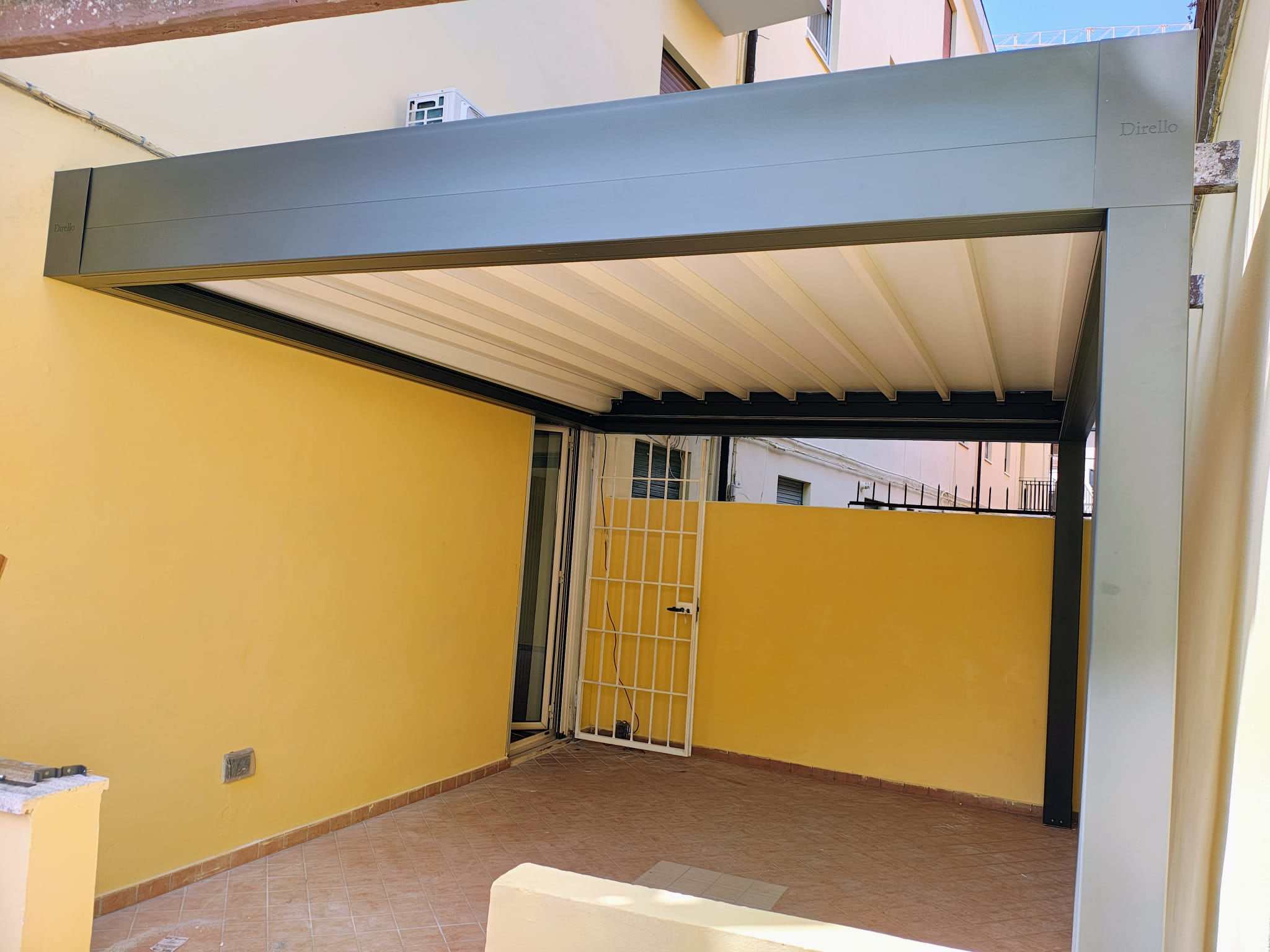 Pergola bioclimatica con telaio antracite e lamelle bianche in un cortile