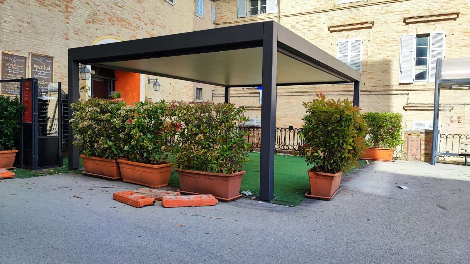 Pergola bioclimatica antracite davanti a un locale in una piazza con palazzi in mattoni