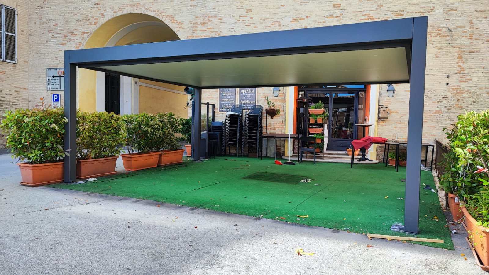 Pergola bioclimatica antracite sul dehors di un locale davanti a un palazzo in mattoni