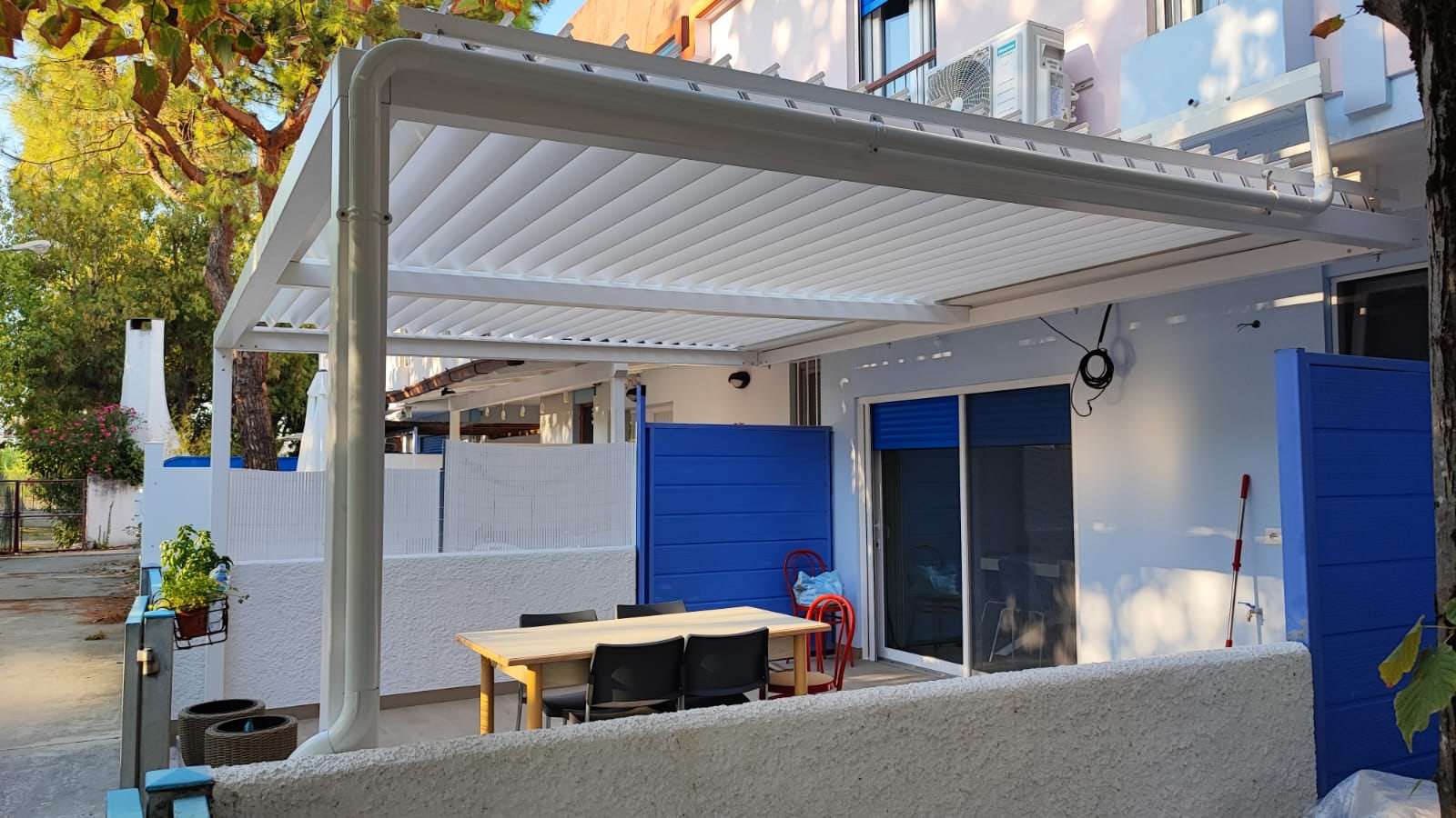 Pergola bioclimatica bianca in un cortile con le lamelle aperte: si vede il cielo tra una lamella e l'altra
