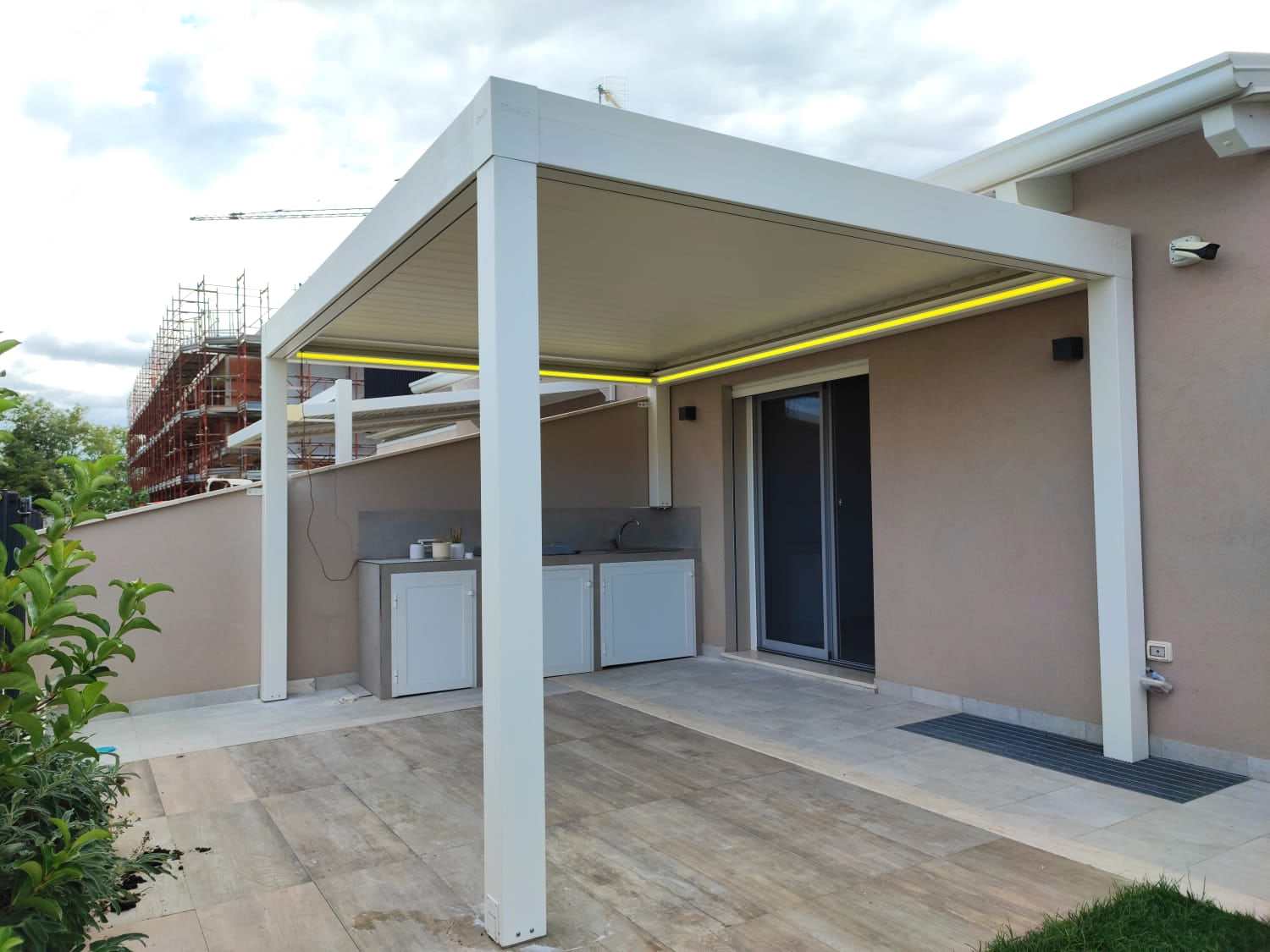 Pergola bioclimatica bianca con striscia LED perimetrale su terrazzo con cucina esterna