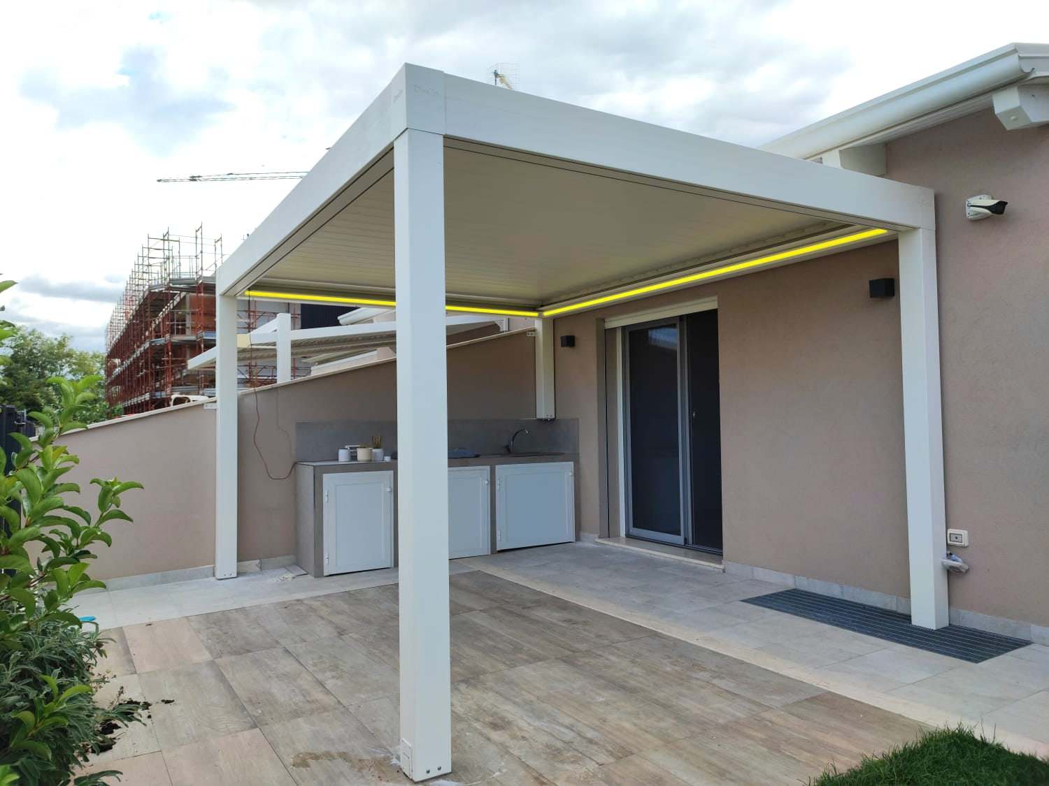Pergola bioclimatica bianca con LED su un terrazzo con cucina esterna