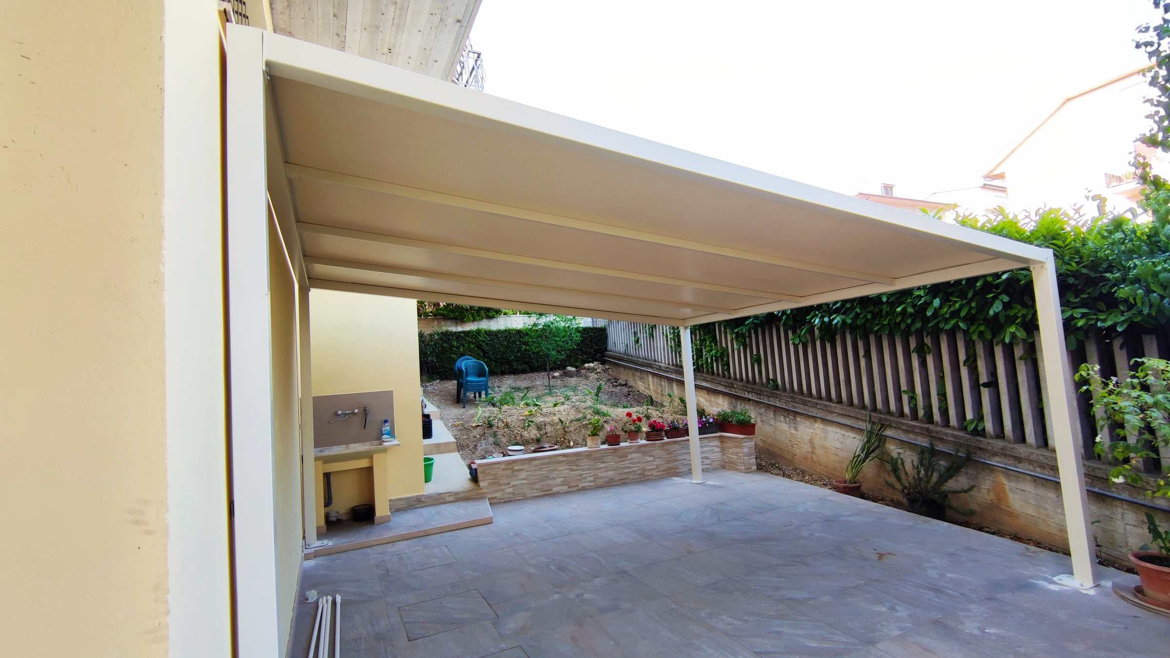 Pergotenda bianca addossata alla casa su un cortile con orto