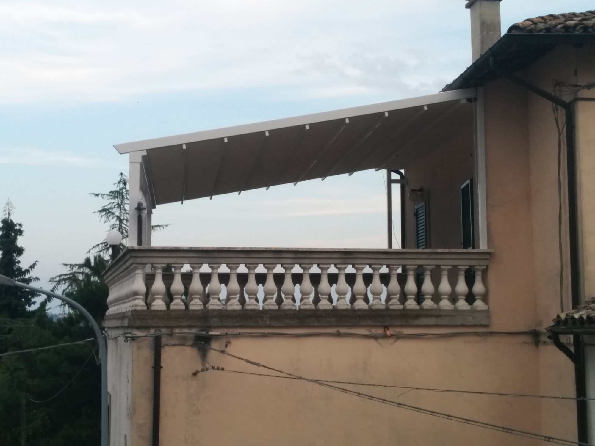 Pergotenda bianca su una terrazza con balaustra in pietra, all'ultimo piano di una casa