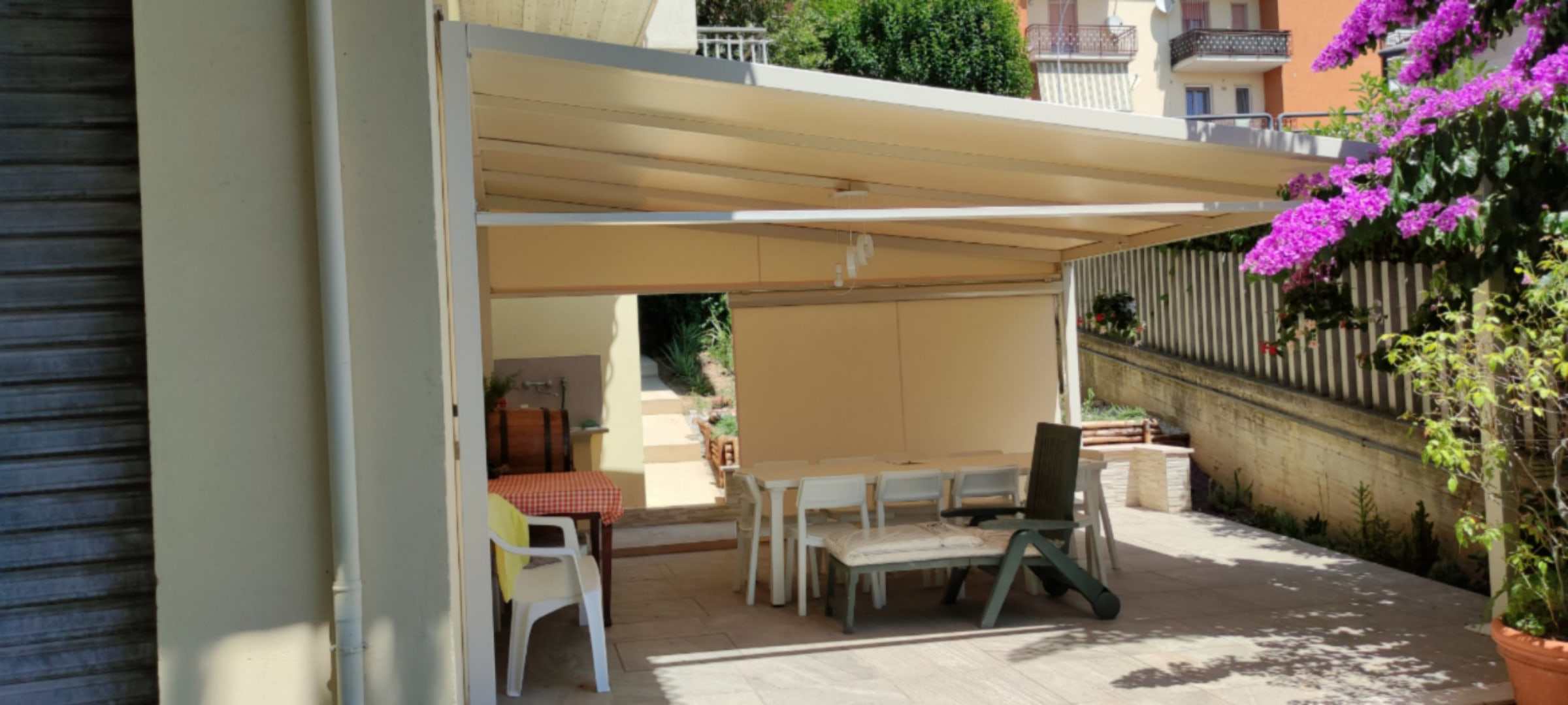 Pergotenda con tende laterali su un cortile con bouganville