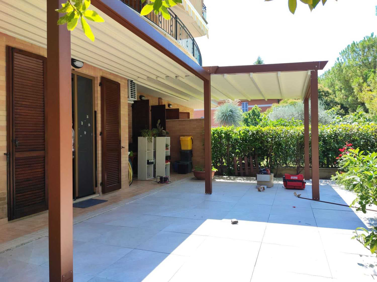 Pergotenda color legno su cortile pavimentato davanti alla casa