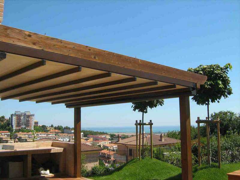 Pergotenda in legno con telo chiaro su un giardino con vista sui tetti e sul mare
