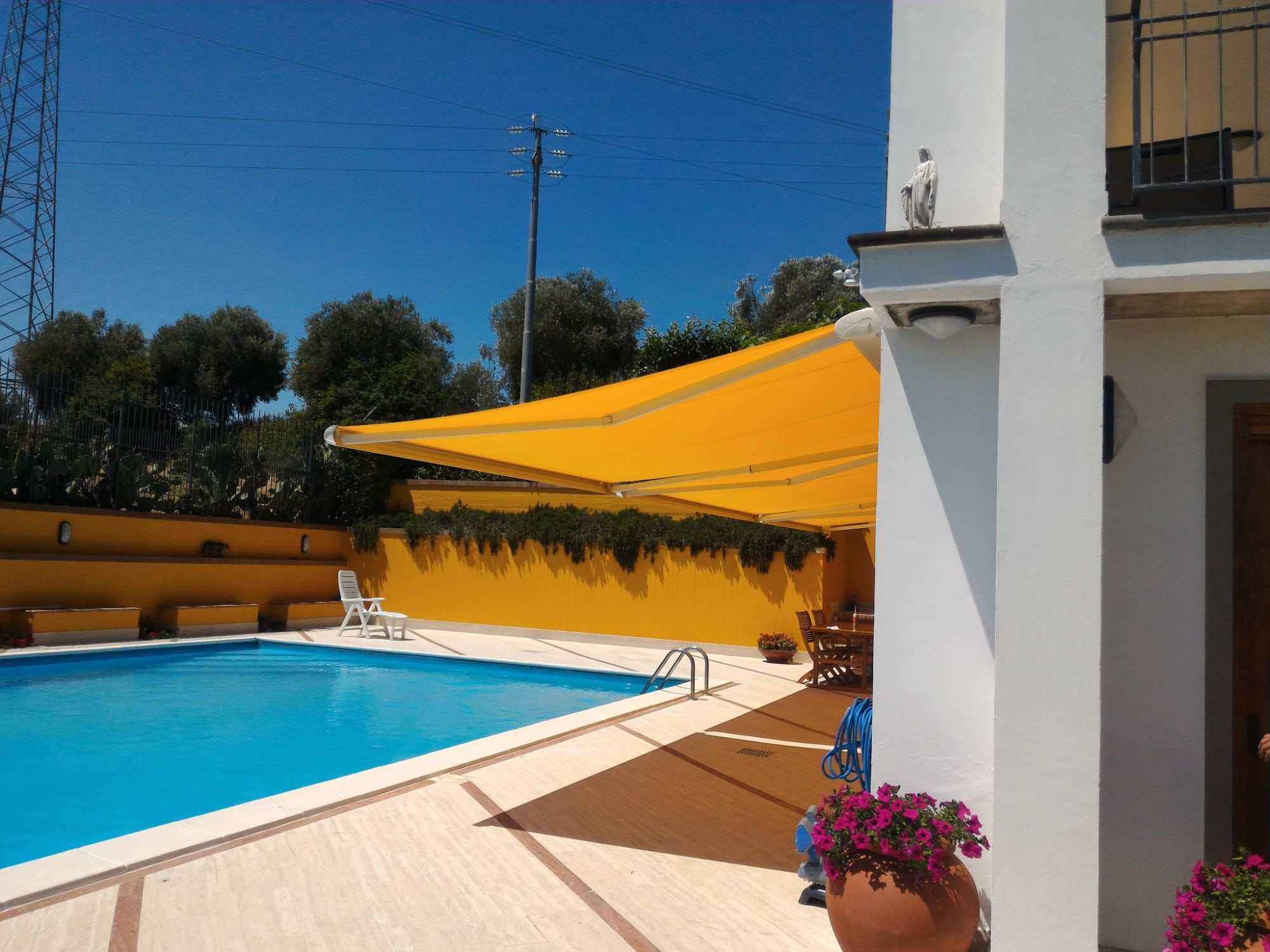 Tenda a bracci con telo giallo aperta sul terrazzo di una villa, accanto alla piscina