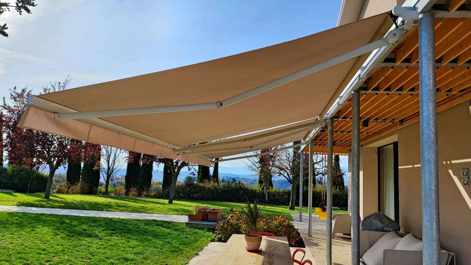 Tenda da sole a bracci estensibili sul portico di una villa con giardino e vista sulle colline