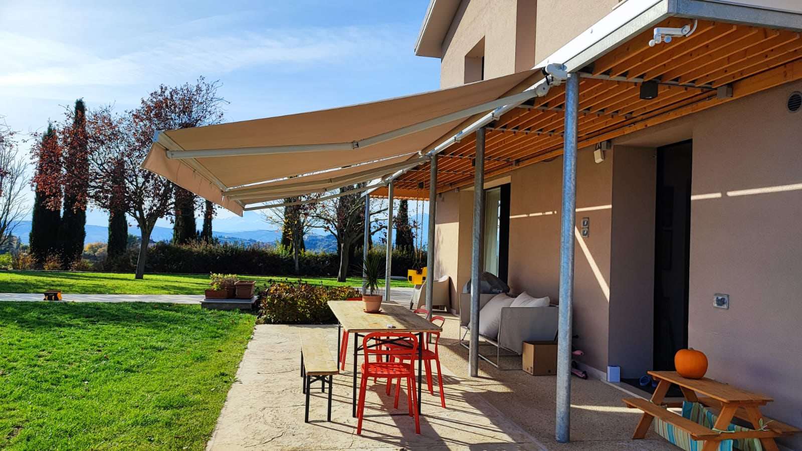 Zona pranzo all'aperto ombreggiata da una tenda a bracci color sabbia