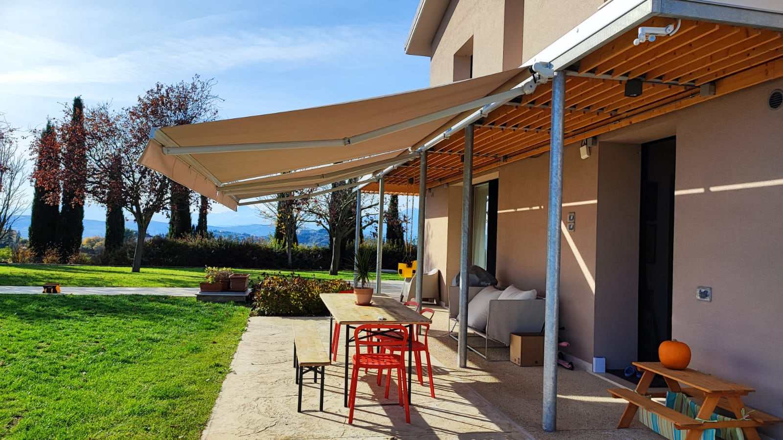 Zona pranzo all'aperto ombreggiata da una tenda a bracci color sabbia