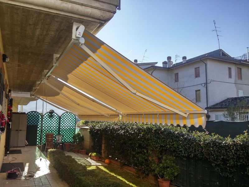 Tenda a bracci a righe gialle su terrazzo con siepe
