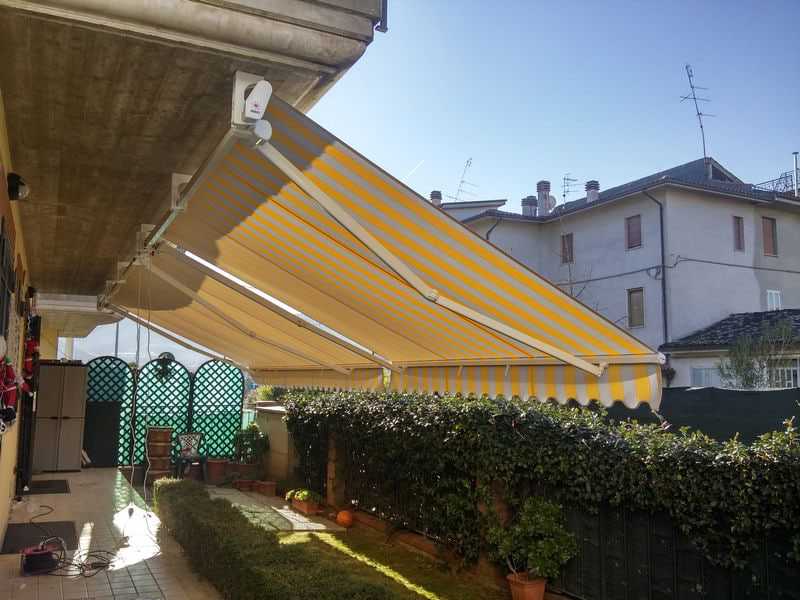 Tenda da sole a bracci con telo grigio aperta su un terrazzo circondato dal verde