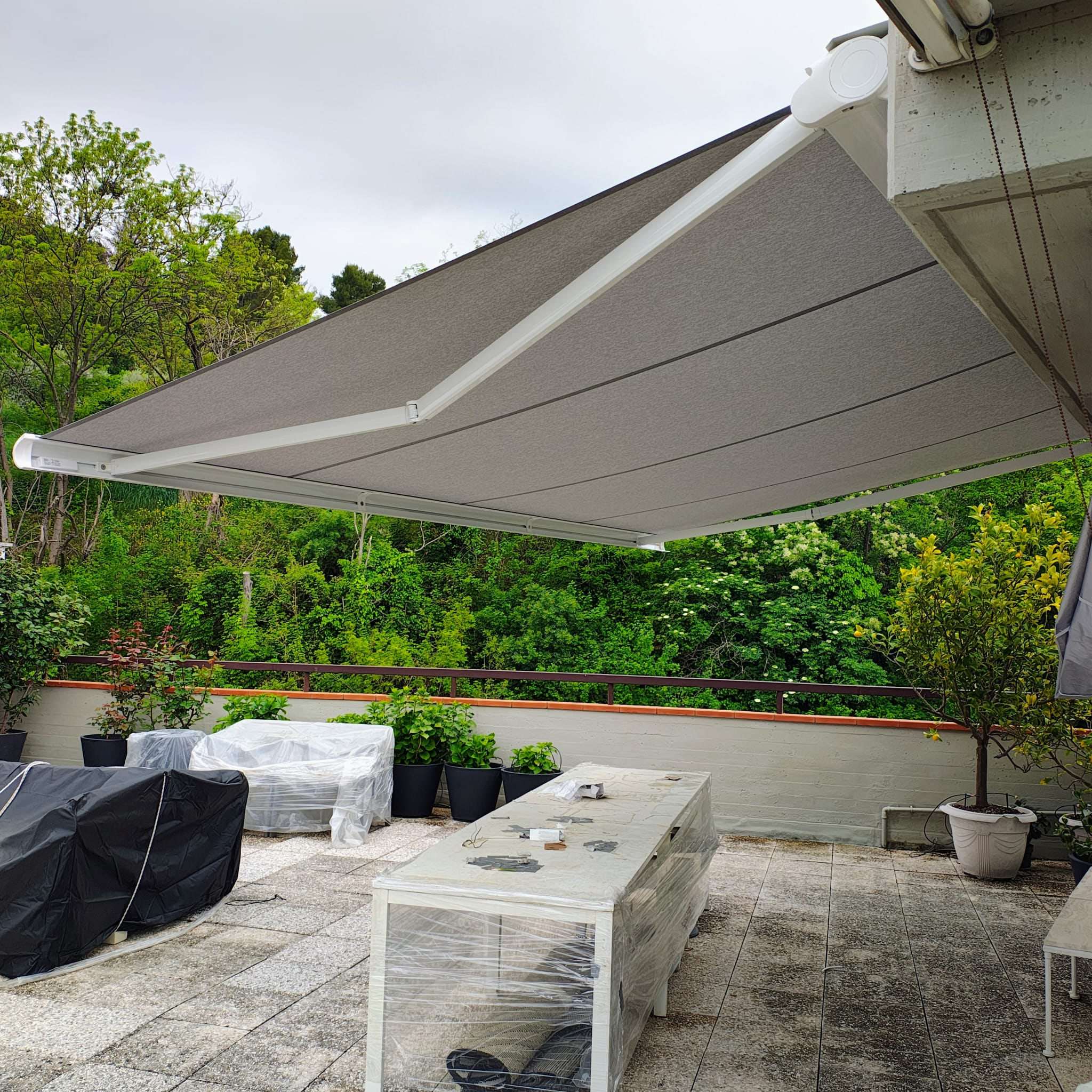 Tenda a bracci color grigio su terrazzo circondato dal verde