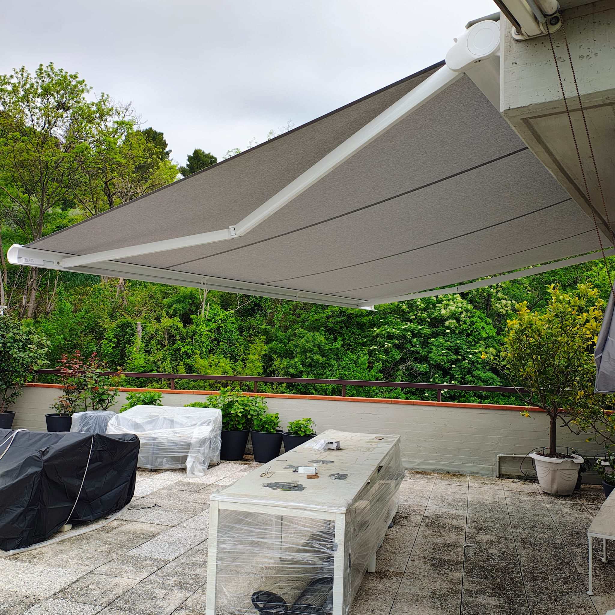 Tenda a bracci color grigio su terrazzo circondato dal verde