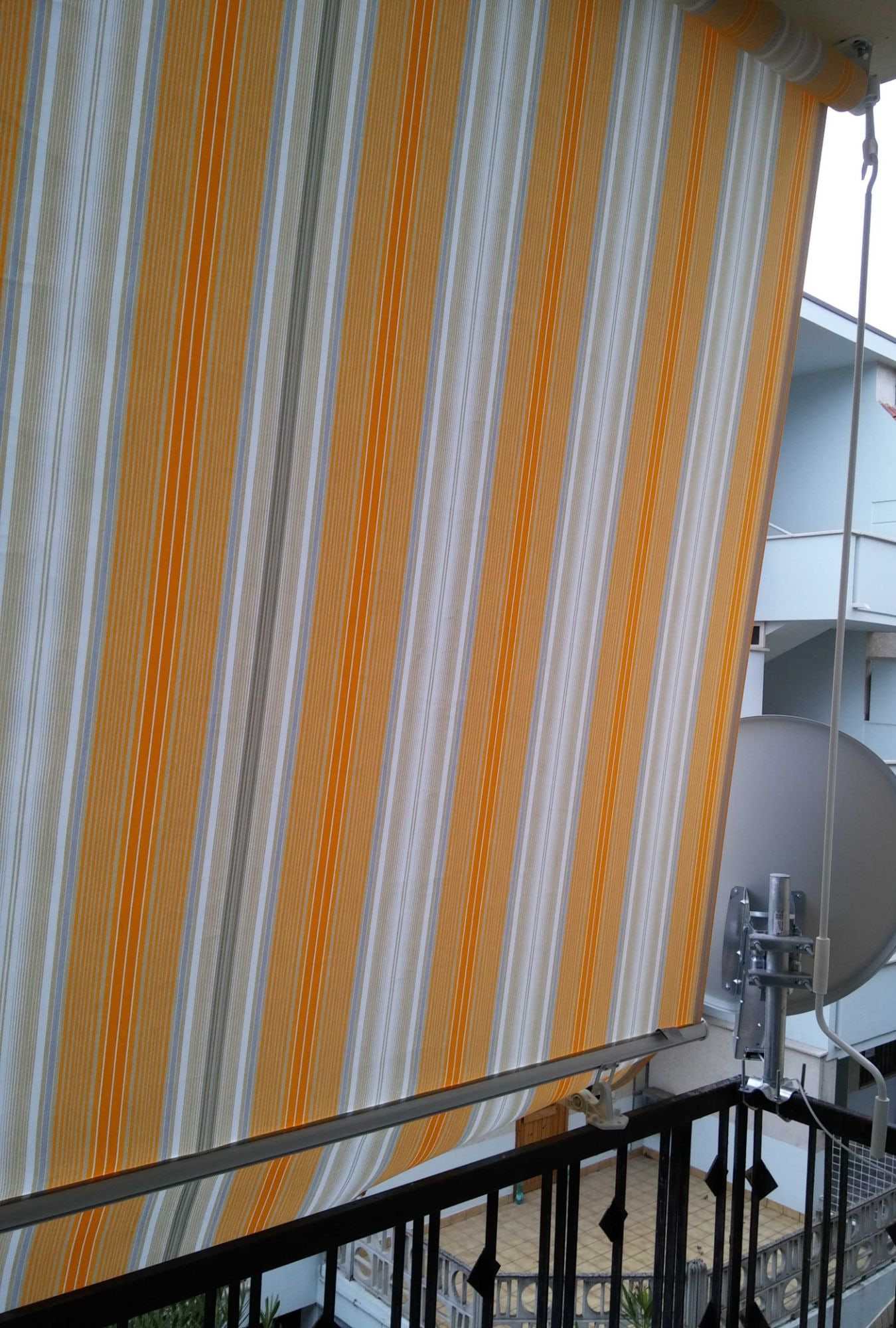 Tenda a caduta a righe arancio, grigie e bianche su un balcone, con asta di manovra ad argano
