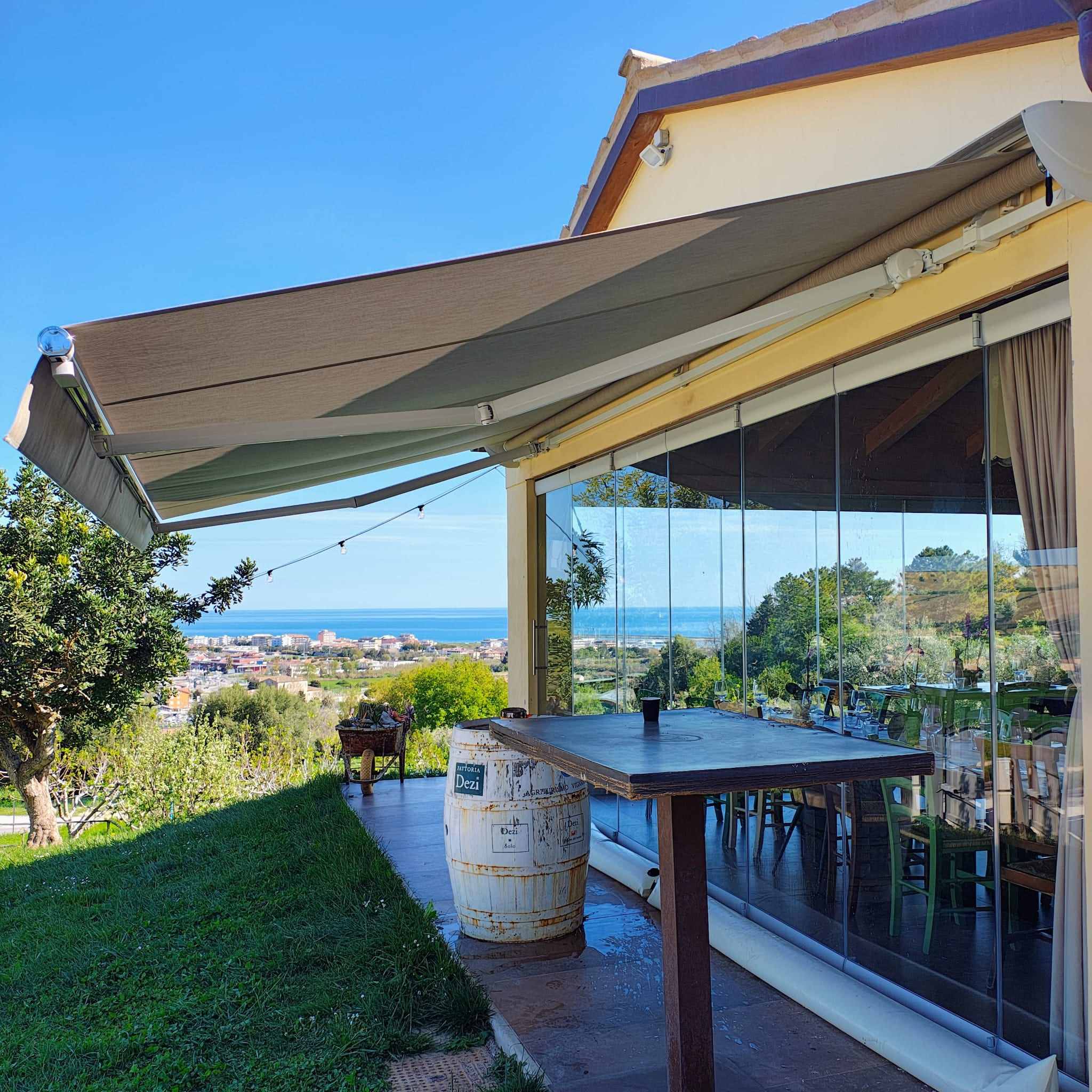 Tenda da sole a bracci e vetrate scorrevoli su un ristorante in collina con vista sul mare Adriatico