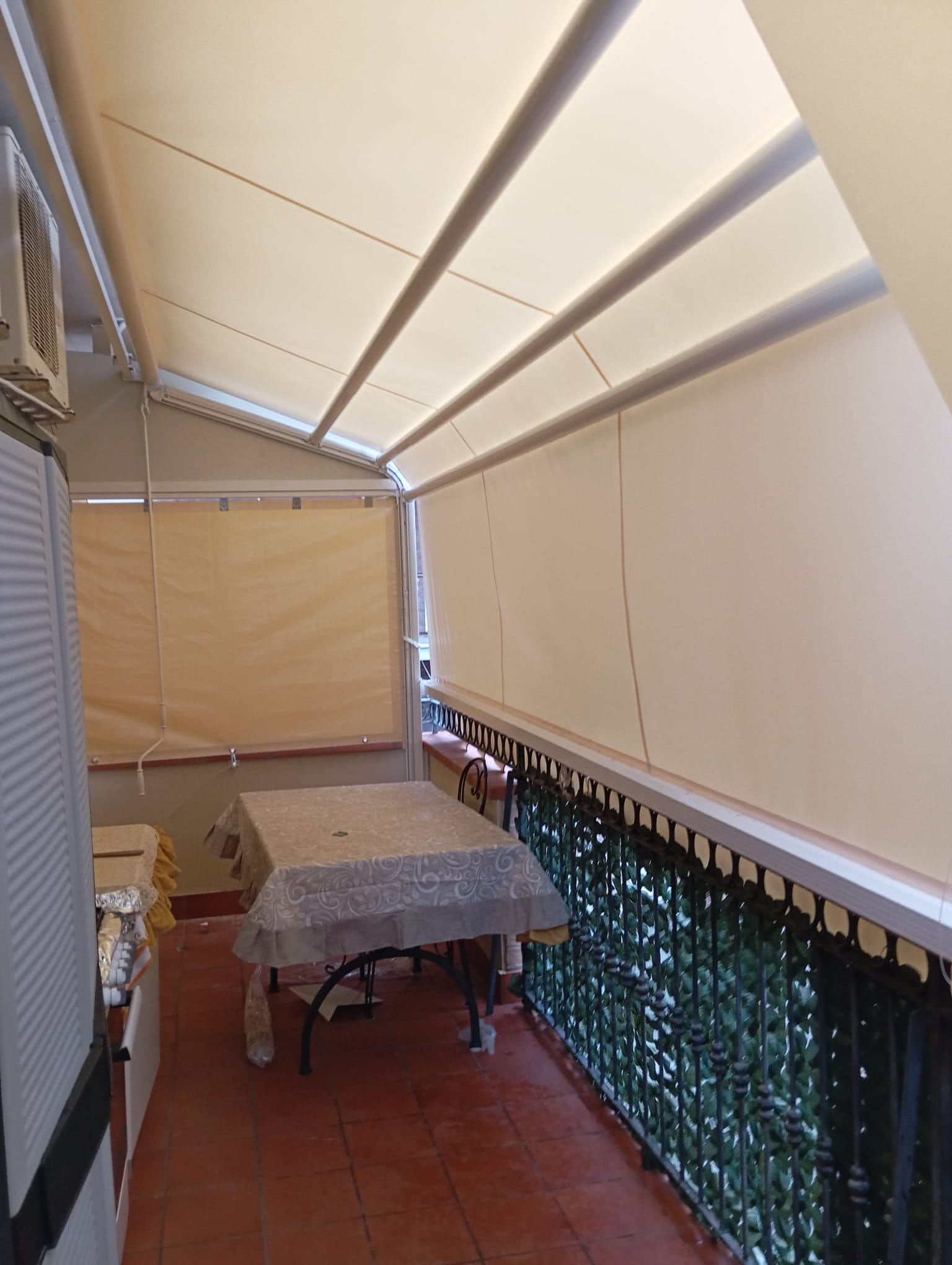 Balcone chiuso da tende verticali a caduta sotto una tenda da sole, vista dall'interno