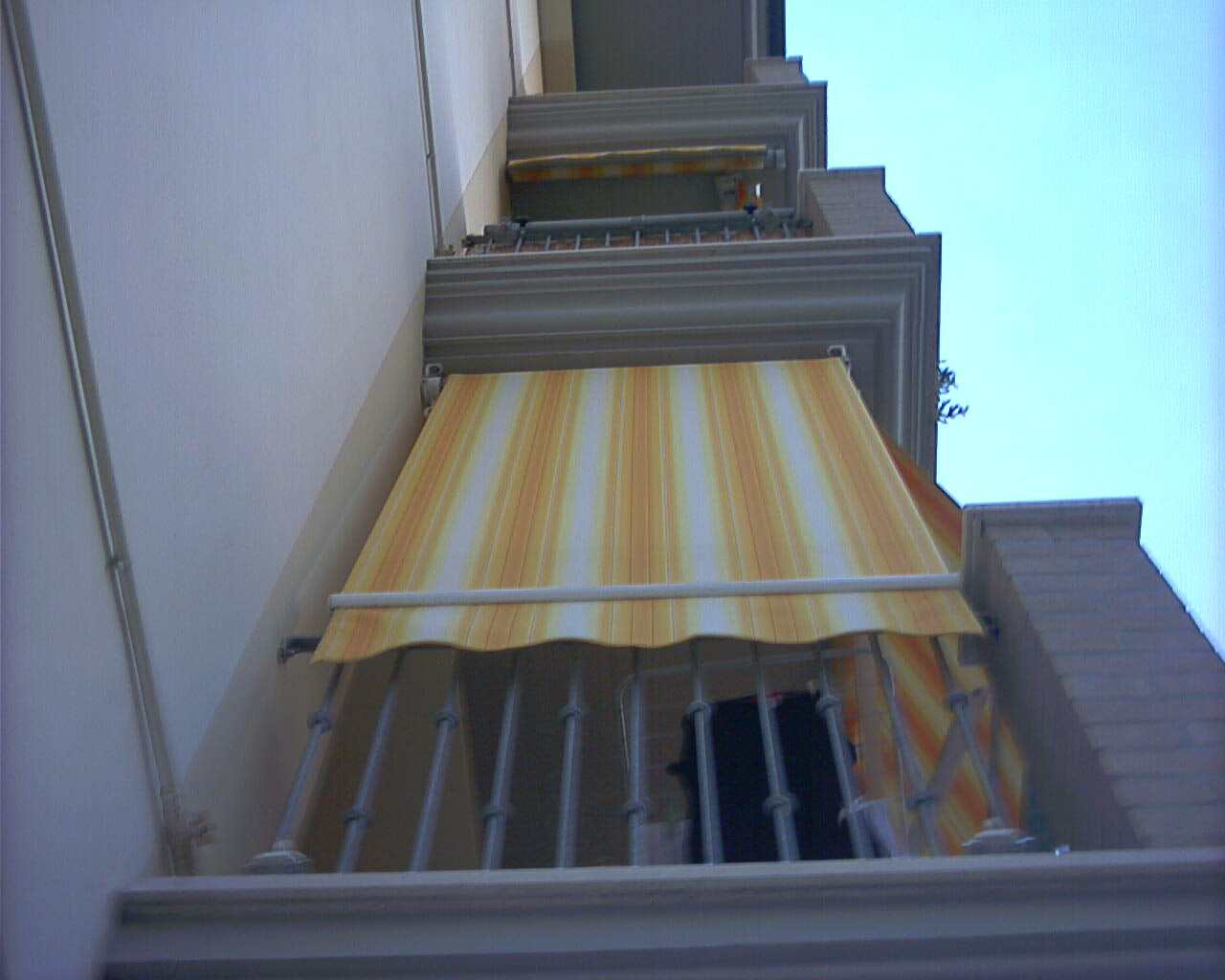 Tende a caduta a righe gialle sui balconi di una palazzina, viste dal basso