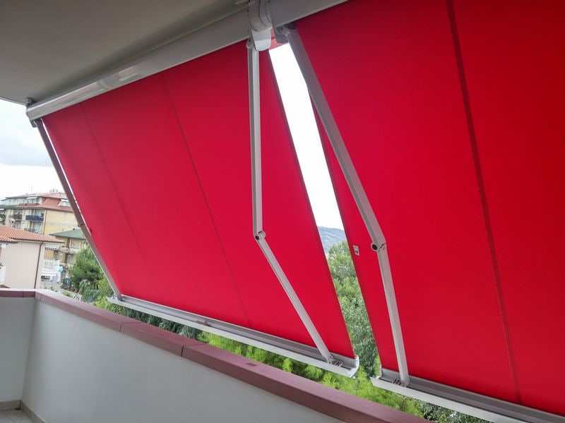 Tende a caduta con braccetti e telo rosso su un balcone