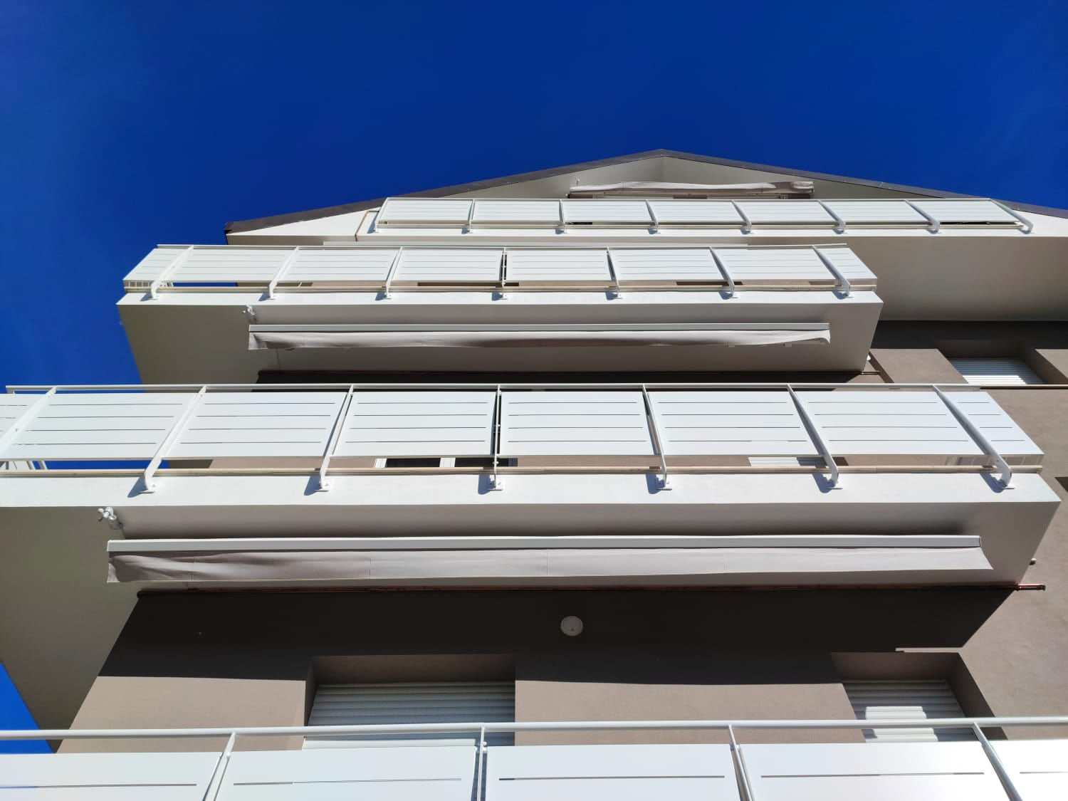 Tende da sole chiuse sotto i balconi di un edificio, cielo blu