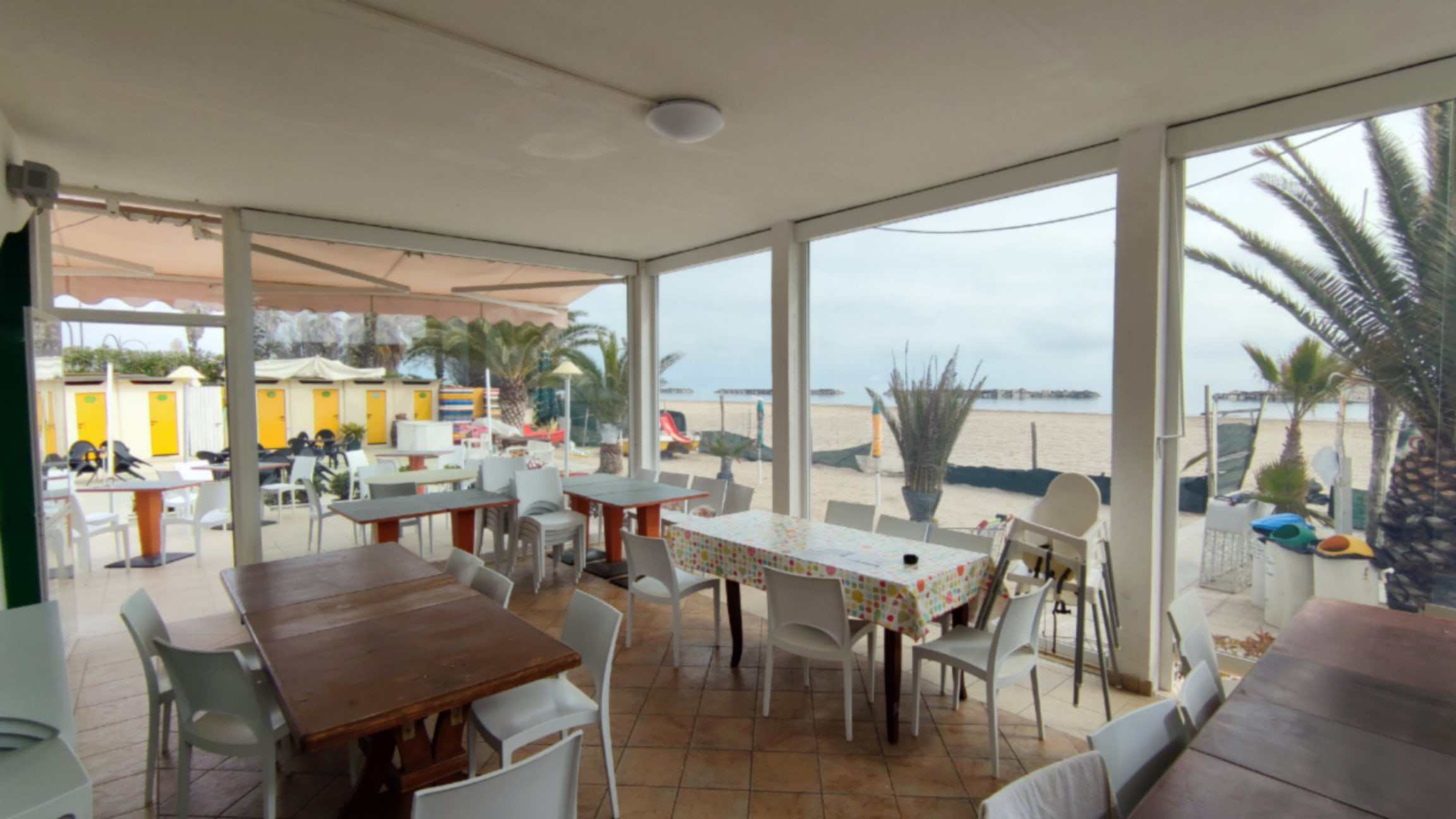 Sala ristorante in spiaggia chiusa da vetrate con vista sul mare