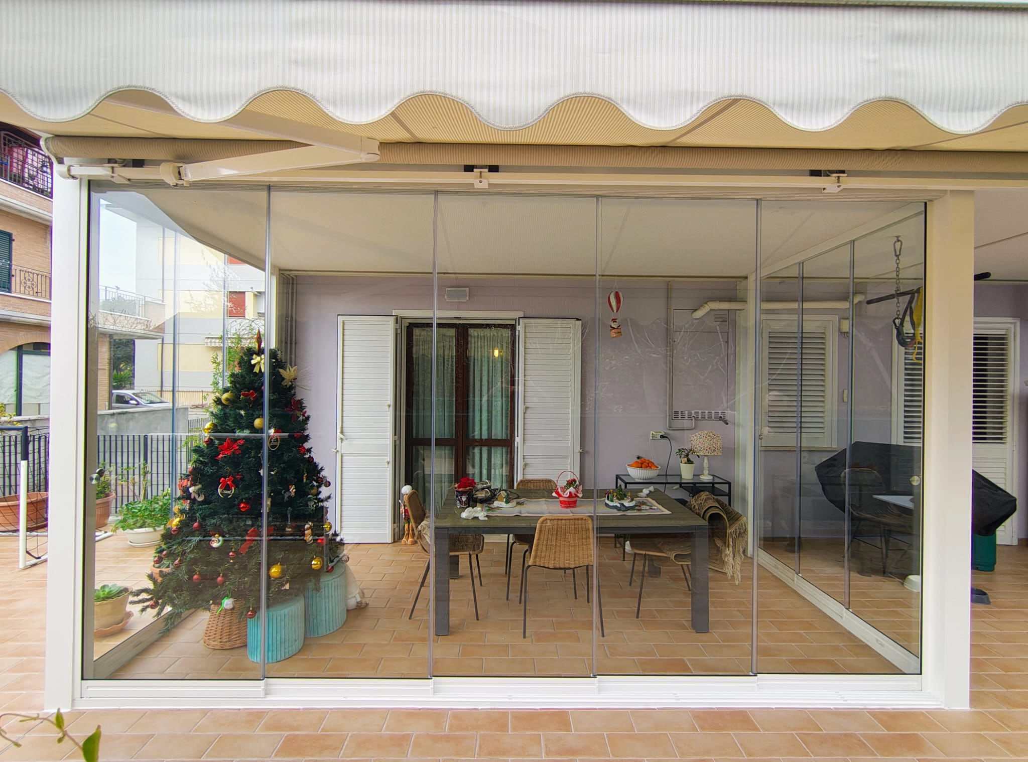 Veranda con zona pranzo chiusa da vetrate scorrevoli sotto una cappottina